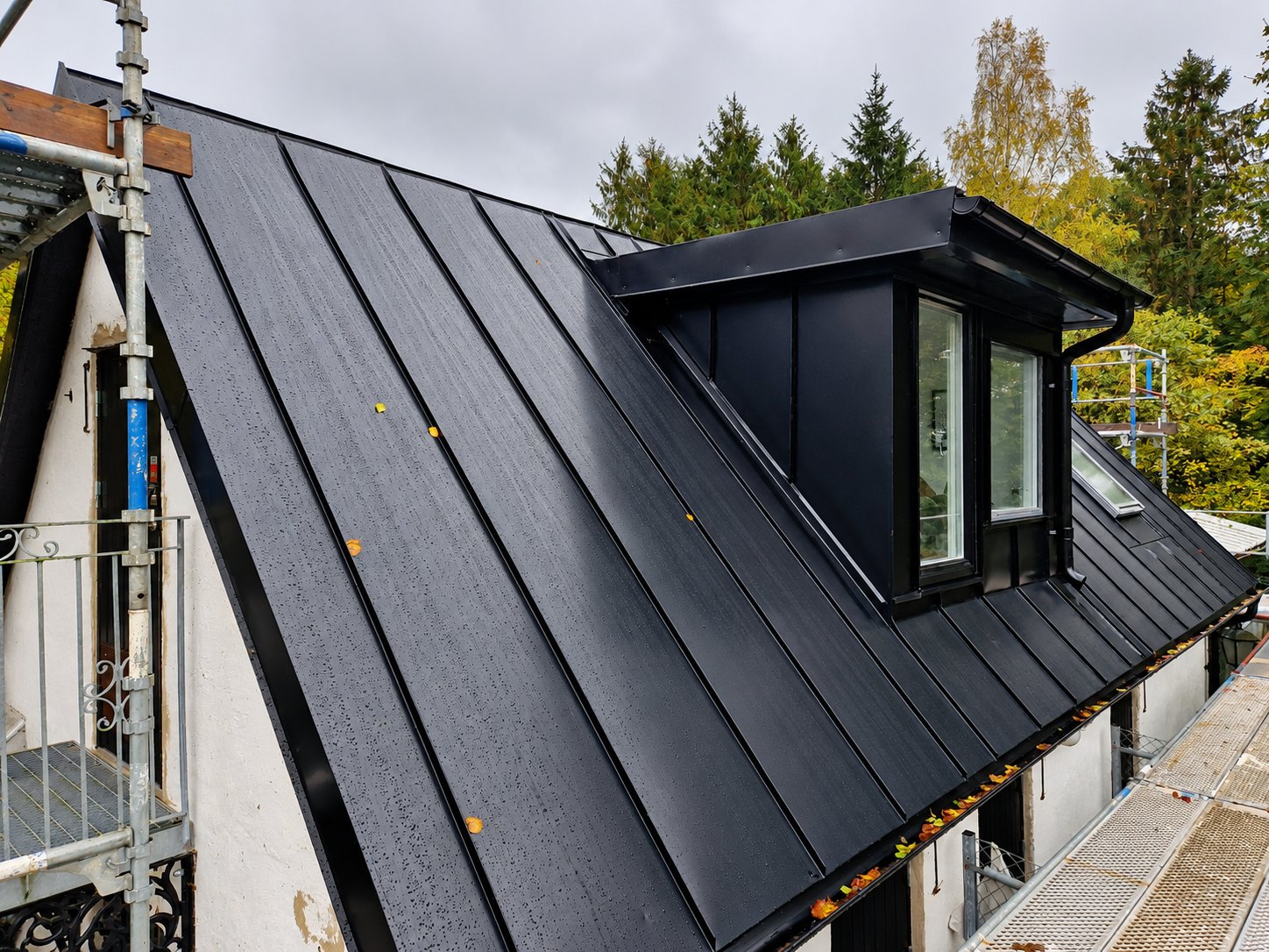 Svart falsat plåttak med plåtklädd kupa på vitputsat hus